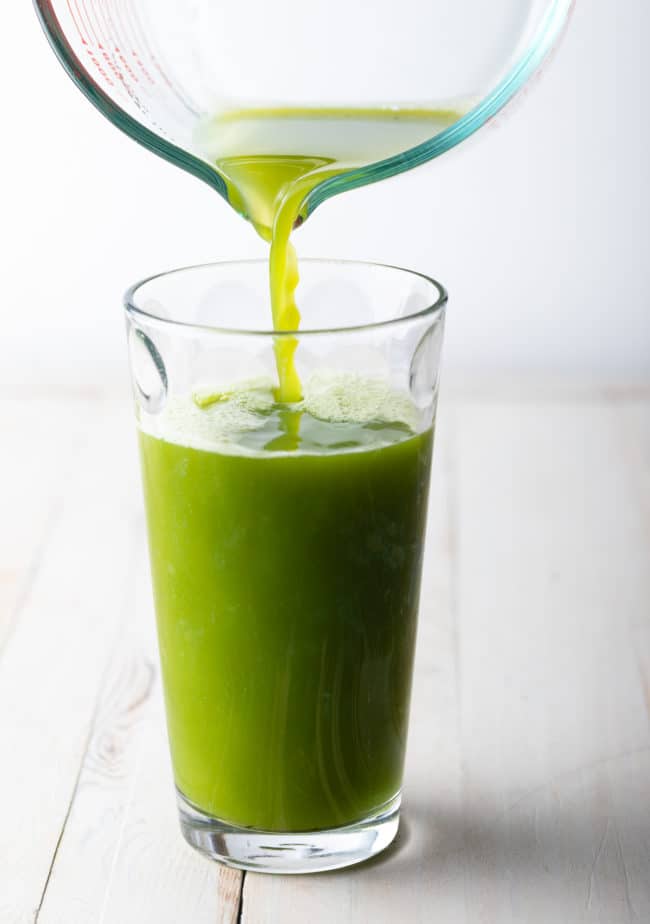 Pouring detox celery juice from a pitcher into a glass. 