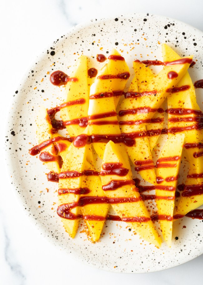 Top down slices of mango on a plate, drizzled with tajin chamoy.