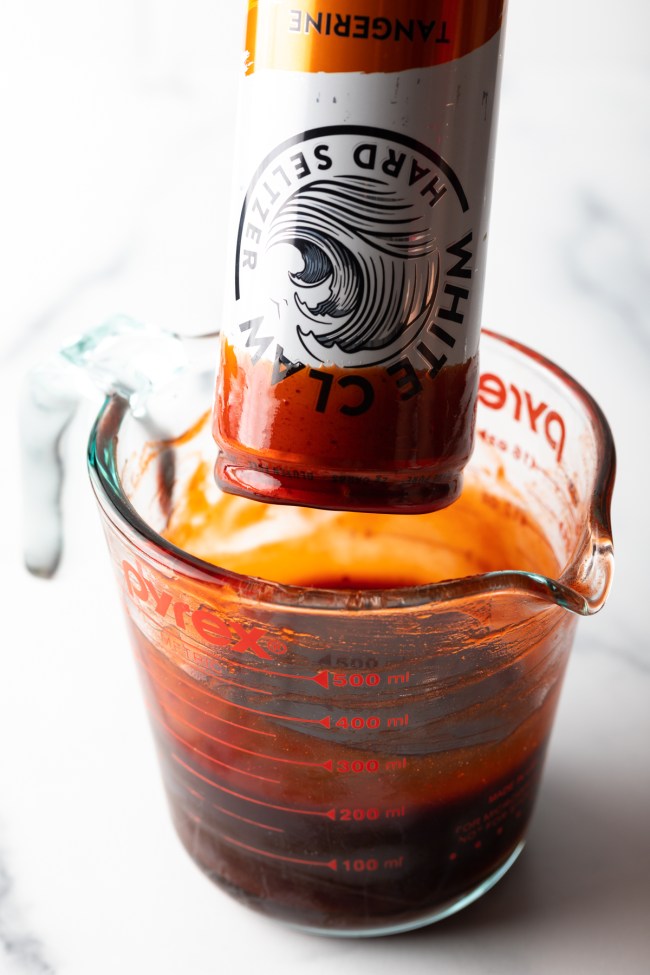 Dipping a white claw can into glass measuring cup with chamoy rim dip.