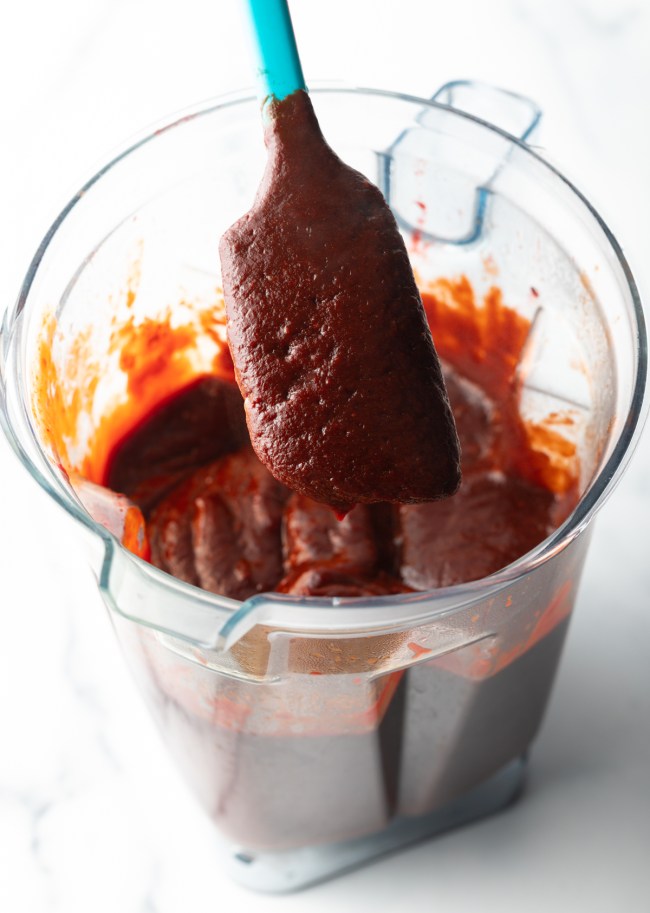 Blue spatula coated in sauce, from a blender jar.