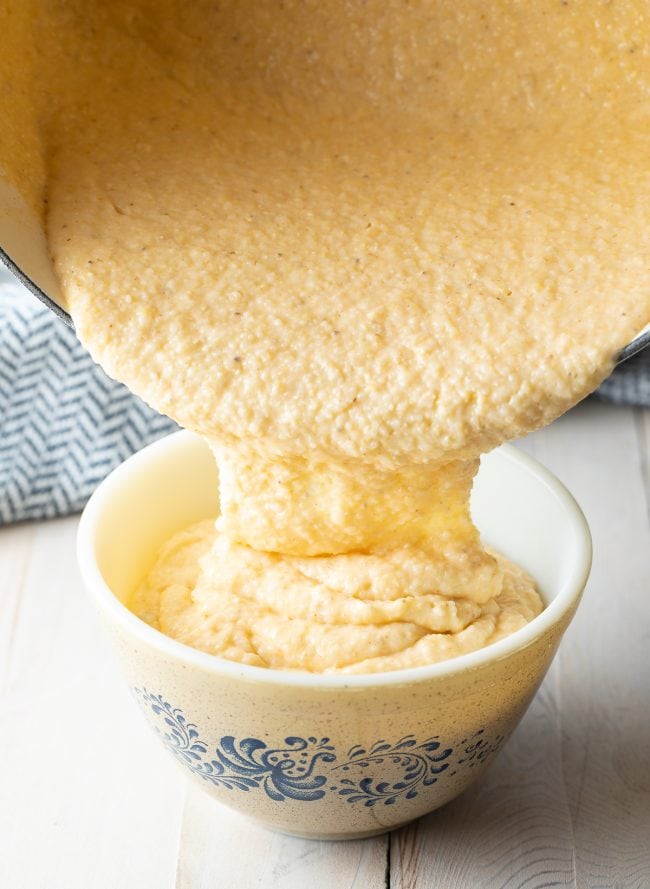 Grits being poured from a pot into a serving bowl. 