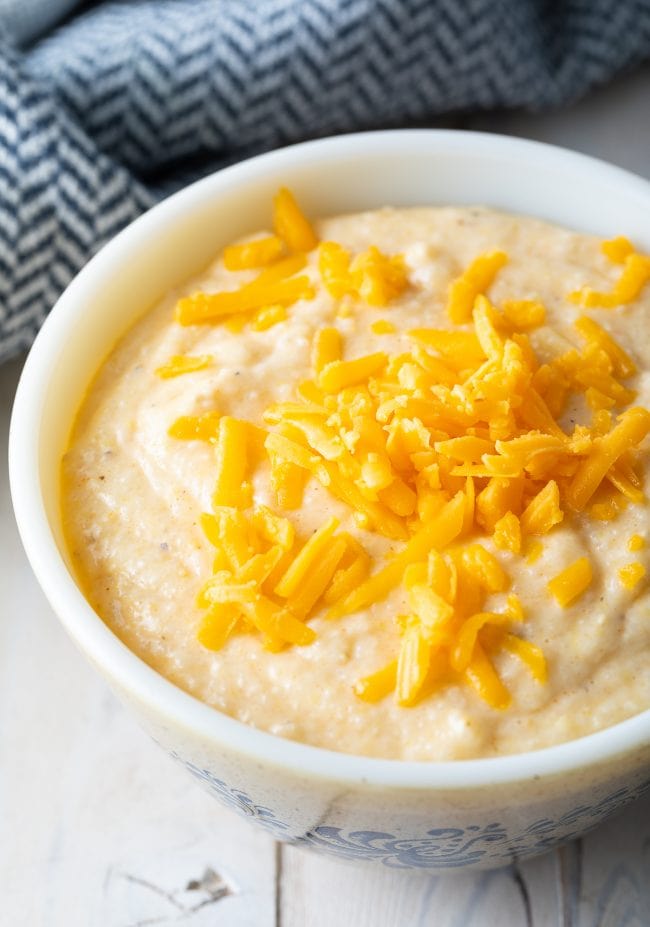 Creamy Cheese grits recipe in a white bowl with shredded cheddar cheese on top. 