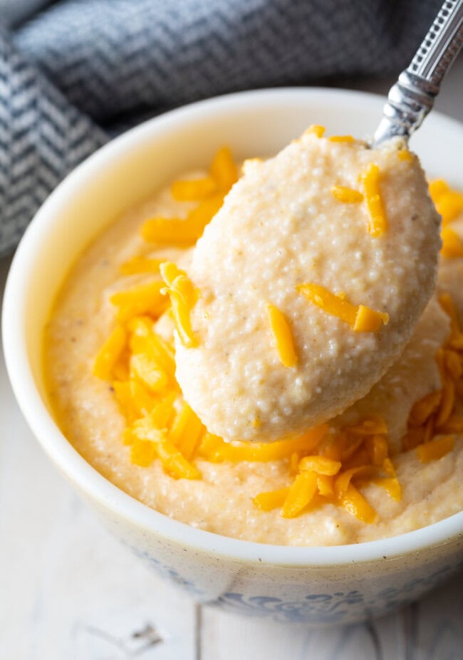 Grits with cheese served in a bowl with a spoon scooping up a bite. 