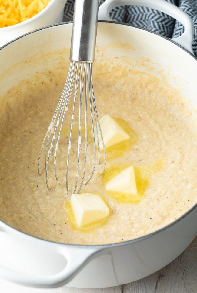 Grits and butter being whisked together in a Dutch oven. 