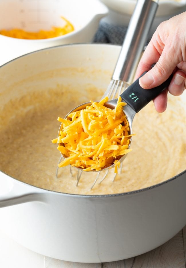 Grits in a stockpot with cheddar cheese being stirred in. 