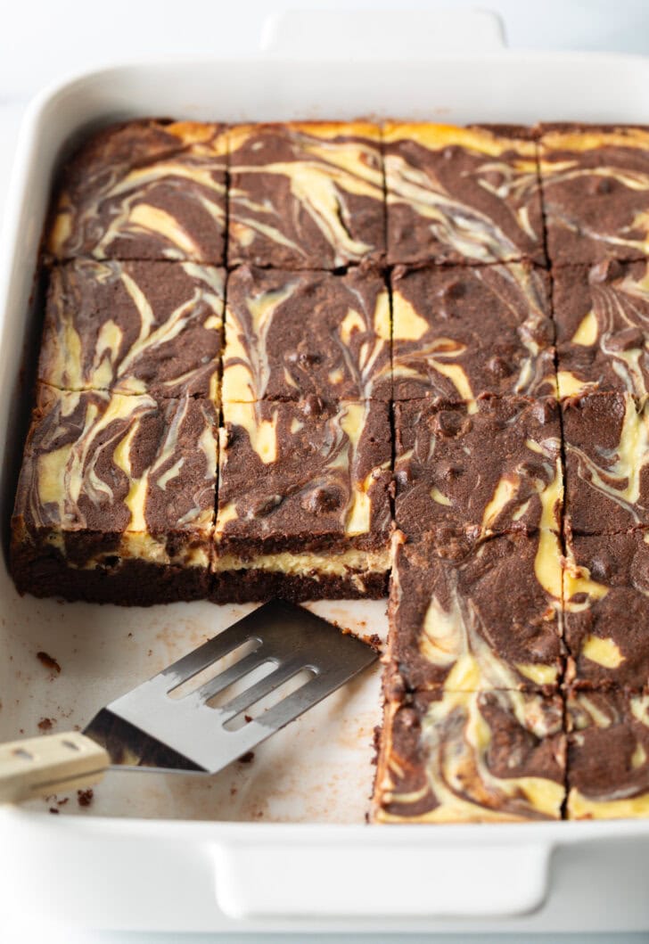 Pan of brownies, a few pieces missing and a metal spatula rests in the pan.