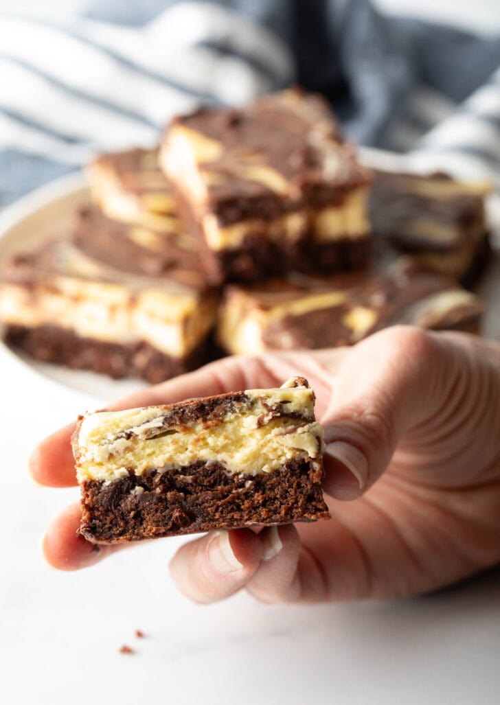 Hand holding cheesecake brownie with bite taken out to camera.