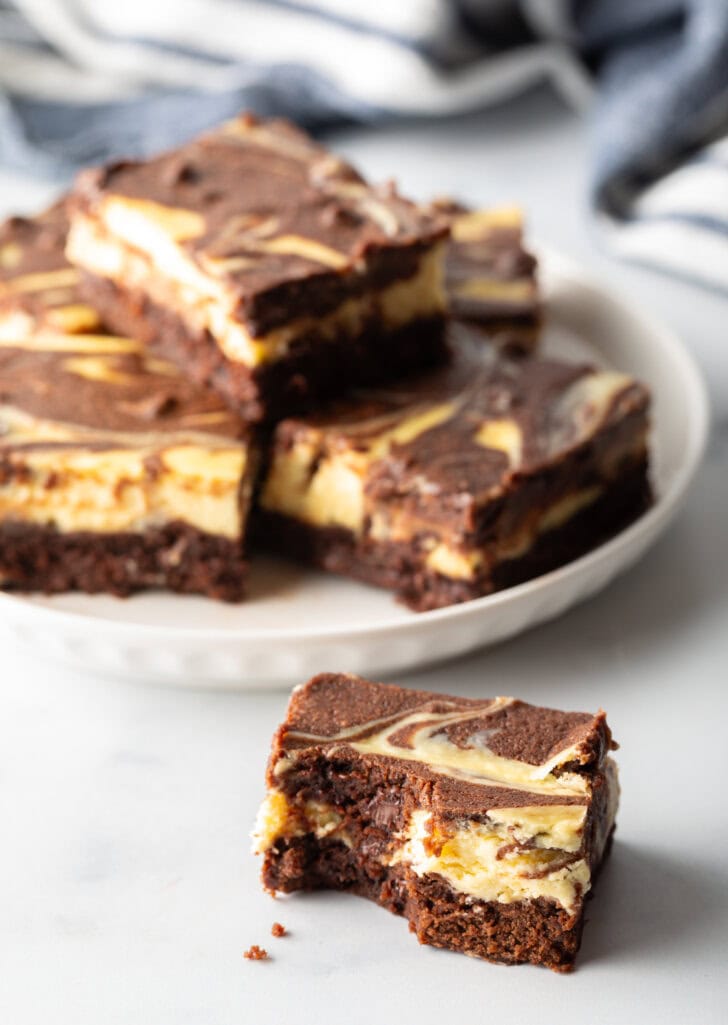 Plate of 5 brownies, one brownie stacked on top. A sixth brownie is placed closer to camera.