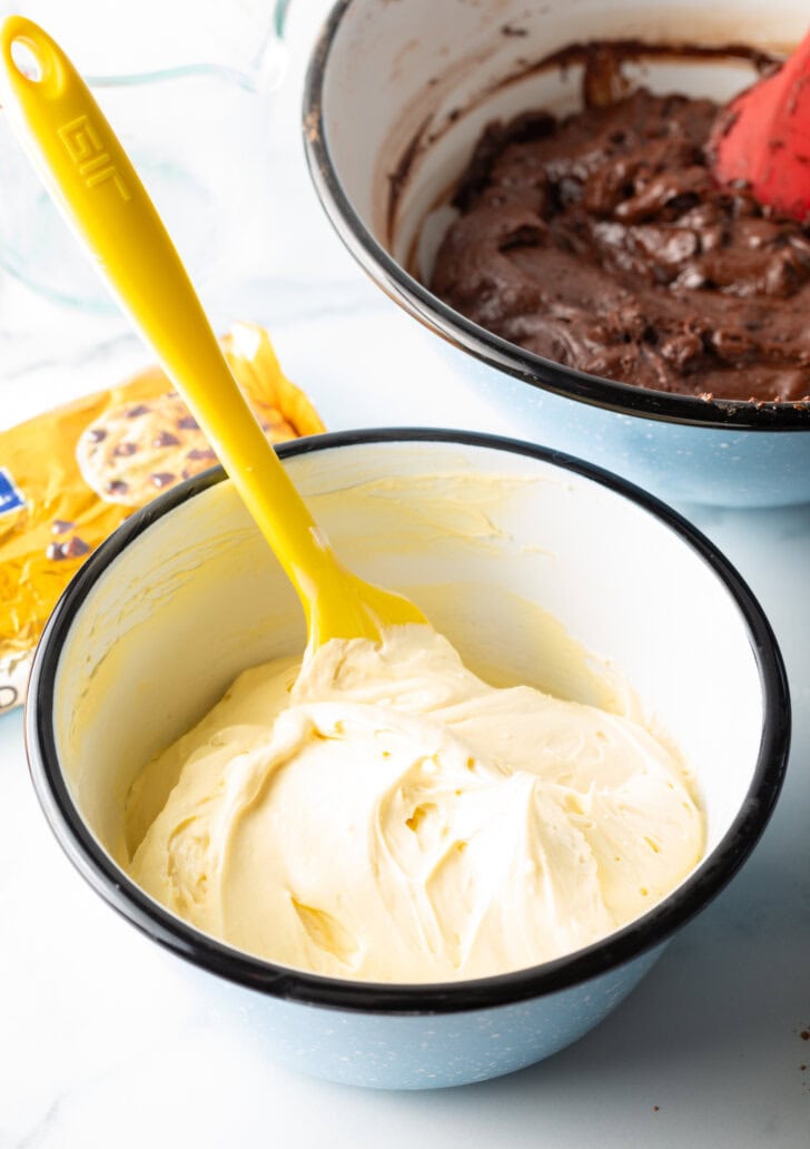 Yellow spatula stirring smooth cream cheese filling in a small white bowl.