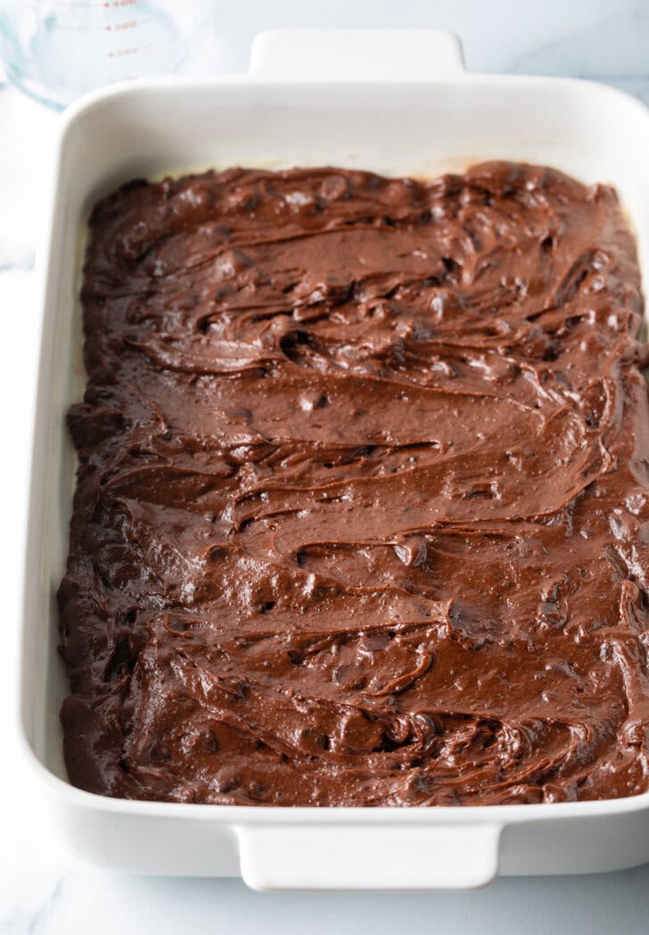 Brownie batter smoothed into a white rectangle baking pan.