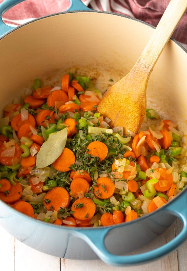 Vegetables sautéing in a soup pot with a wooden spoon. 