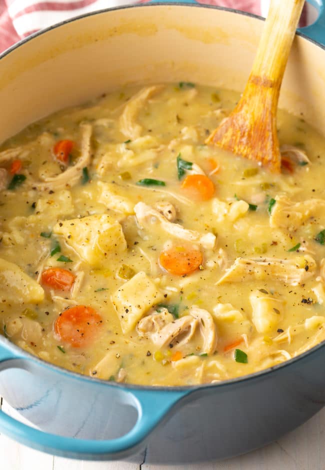 Chicken and dumplings in soup form in a large pot with a wooden spoon.