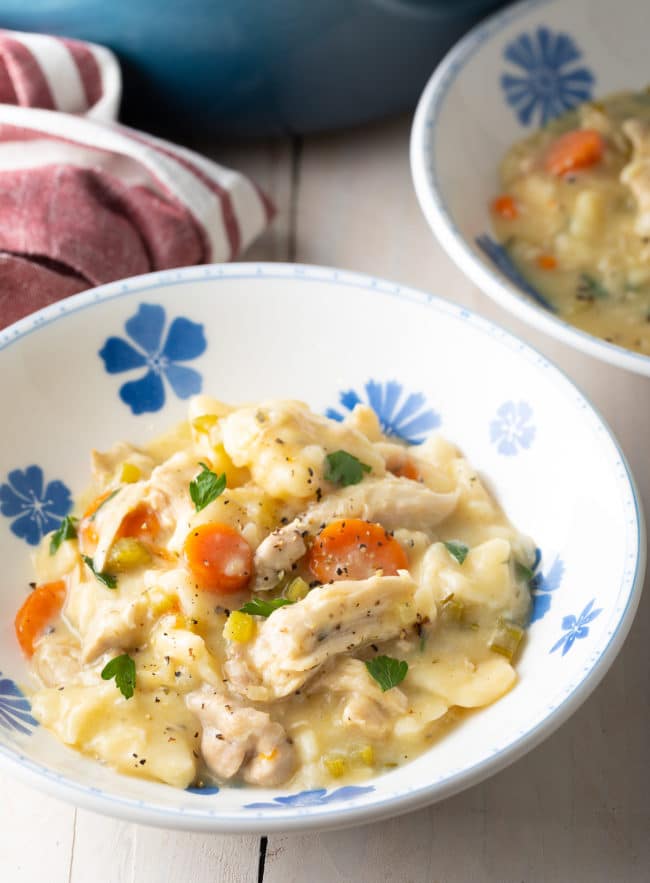 Thick chicken and dumplings served in a bowl with a sprinkle of pepper on top. 
