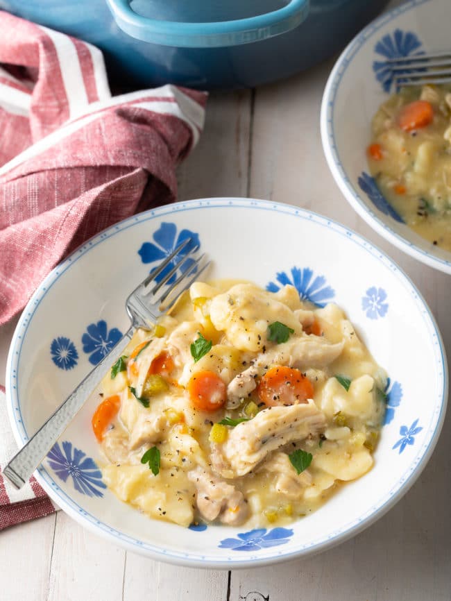 A full serving of dumplings with chicken in a bowl with a fork. 
