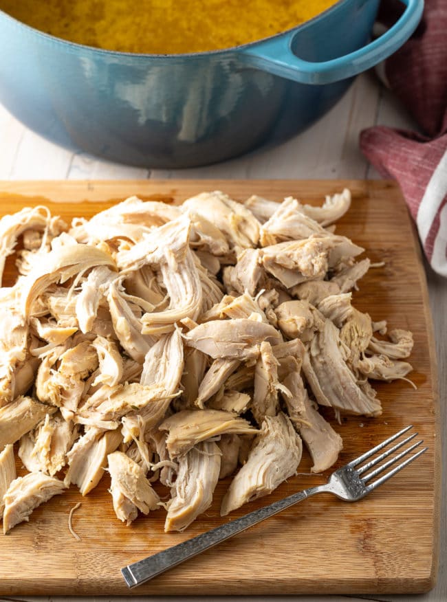 Pieces of shredded chicken that have been pulled off the bone on a wooden cutting board. 
