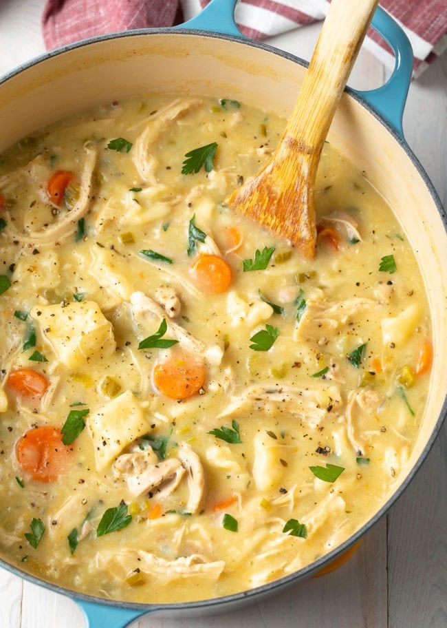 Chicken and dumplings in a large dutch oven pot with a wooden spoon. 