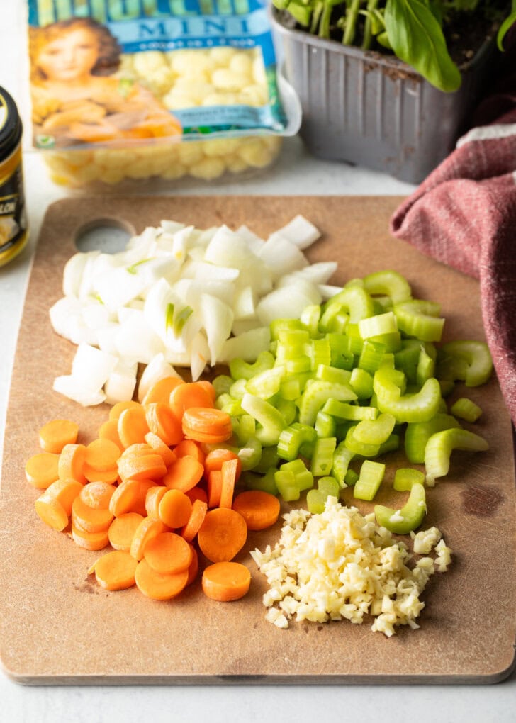 Soup recipe ingredients: Individual chopped piles of carrots, celery, onion, and garlic on a cutting board.