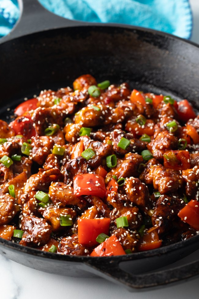 Side view final chicken manchurian in a skillet, topped with green onion slices and sesame seeds.