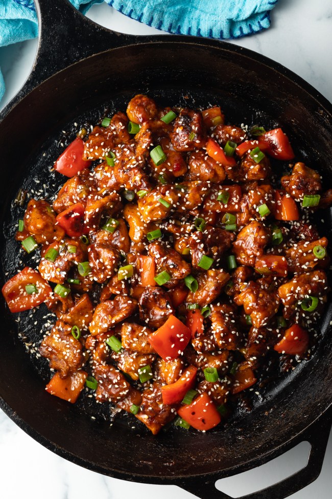 Top down view final chicken manchurian in a skillet, topped with green onion slices and sesame seeds.