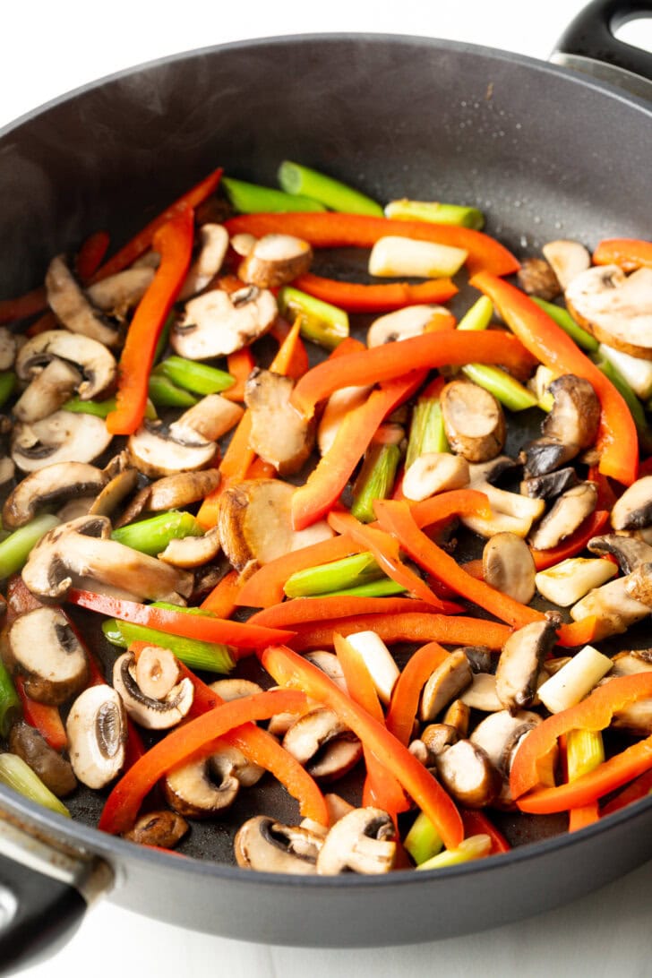 Stir frying sliced bell peppers, mushrooms, and snap peas in a large skillet.