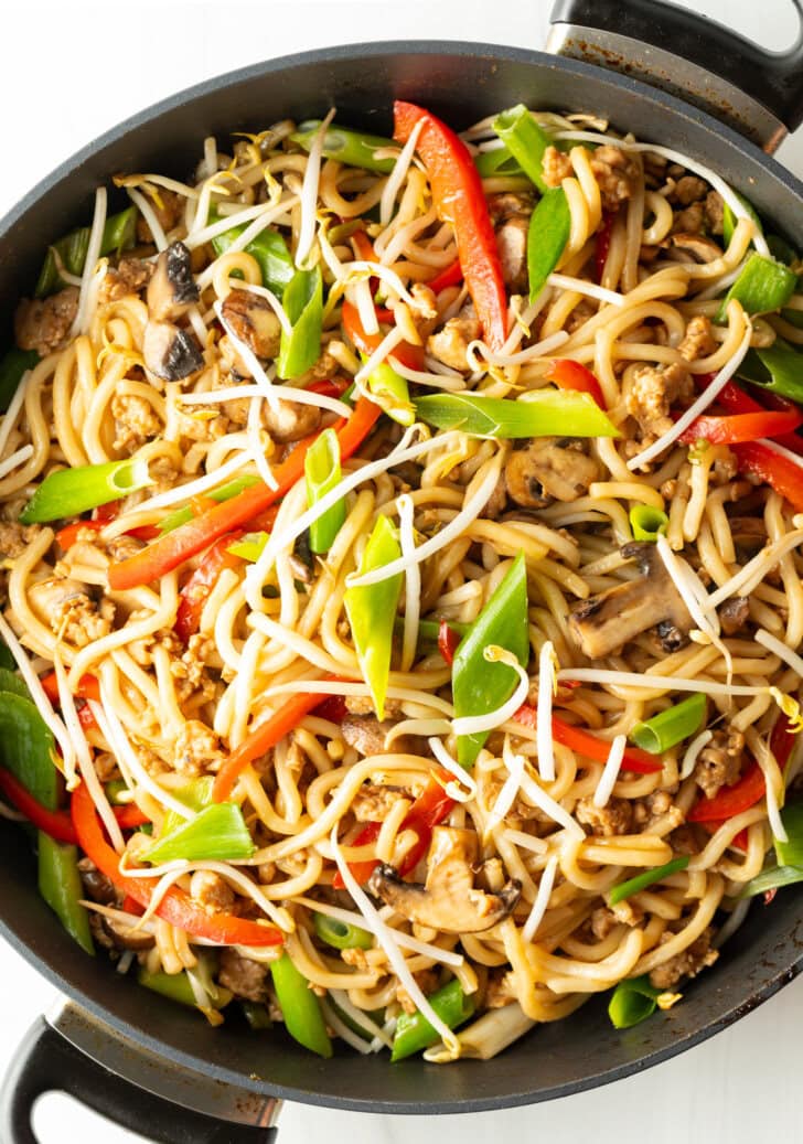 Top down view of a skillet of chicken yaki udon topped with green scallion slices and mung beans.