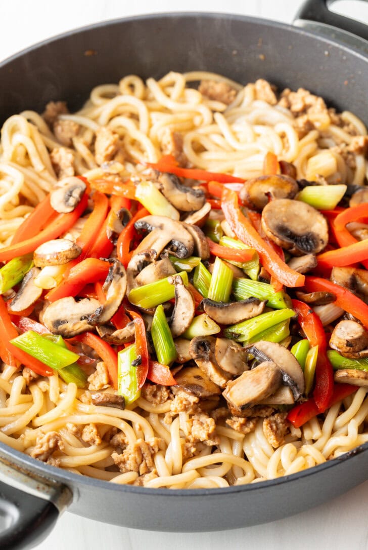 Adding stir fried veggies back to the skillet with noodles and chicken.