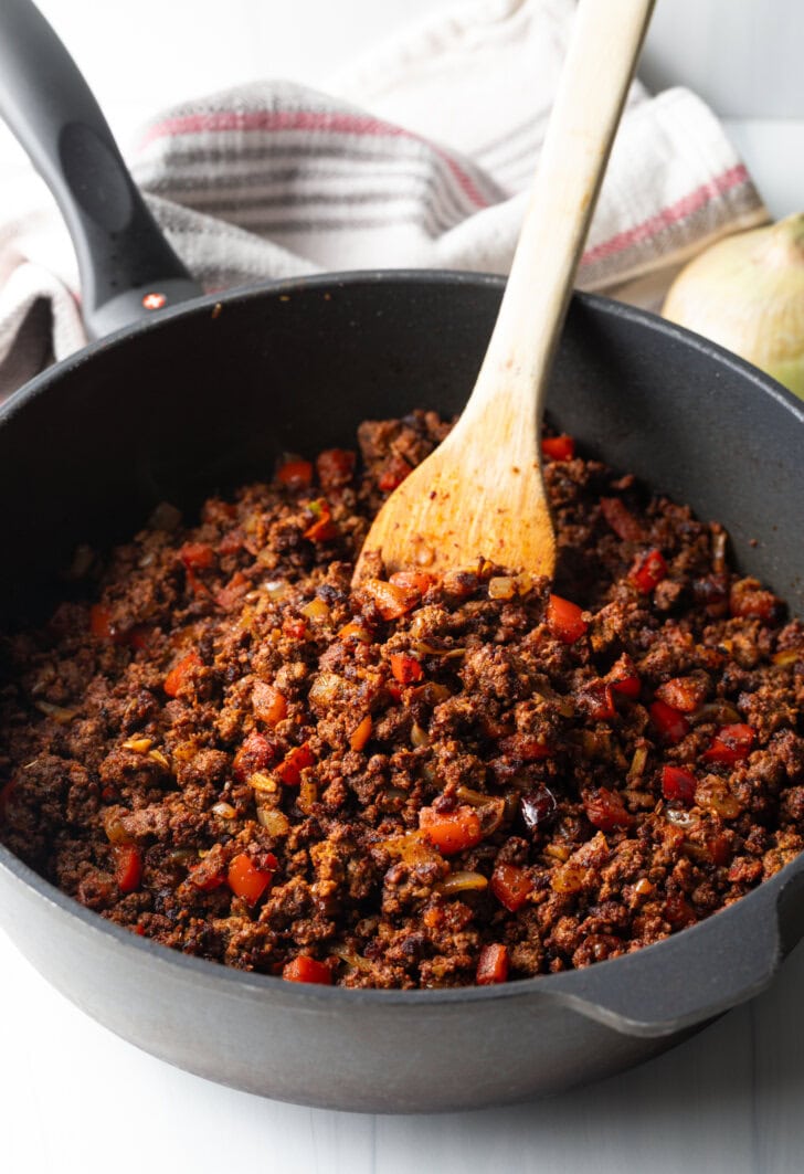 Wooden spoon stirring chili in a deep cast iron skillet.