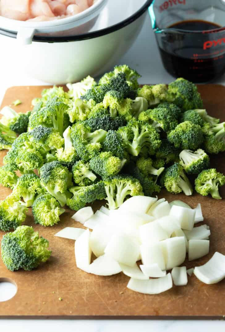 Piles of chopped white onion and fresh broccoli florets on a cutting board.