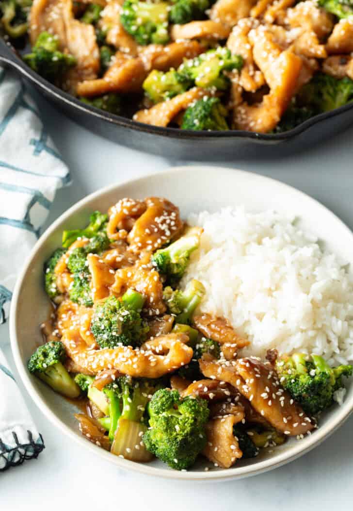 White shallow bowl with serving of Chinese chicken and broccoli with white rice.