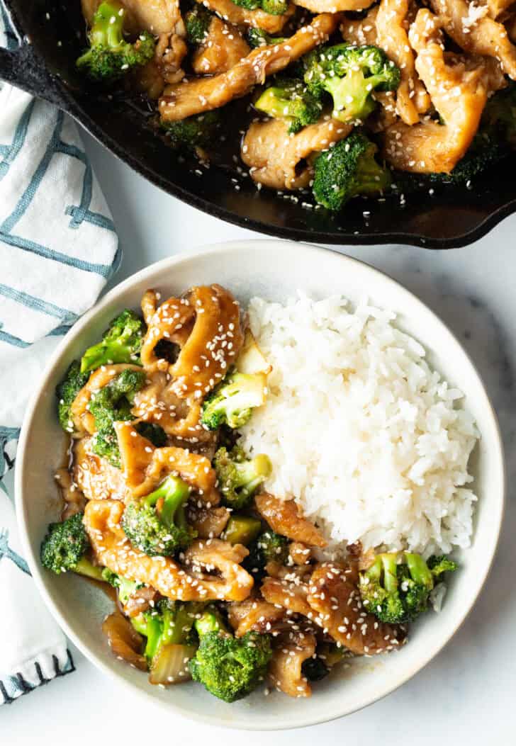 White shallow bowl with serving of Chinese chicken with broccoli with white rice.