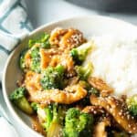 White shallow bowl with serving of Chinese chicken and broccoli with white rice.