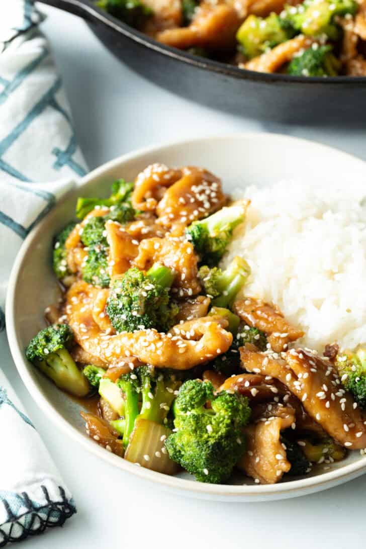 White shallow bowl with serving of Chinese chicken and broccoli with white rice.