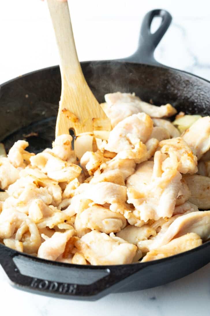 Cooking pieces of chicken in a black cast iron skillet with a wood spatula.