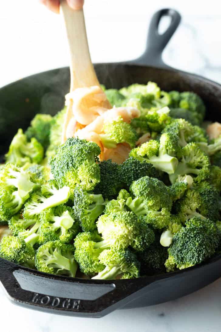 Stirring fresh broccoli florets into the dish.