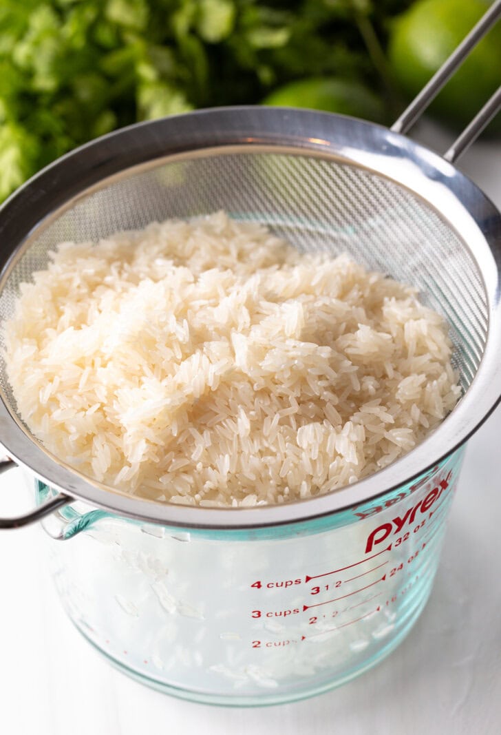 Straining white rice over a glass measuring pitcher.