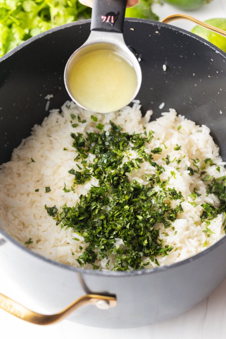 Adding lime juice from a measuring spoon over a pot with rice and chopped cilantro.