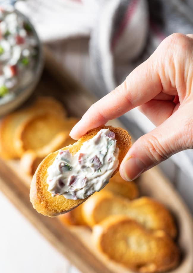 Hand holding a small piece of bread with dried beef dip spread on top. 