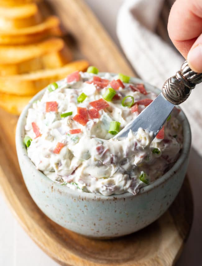 Hand holding a butter knife being dipped into the dip. 