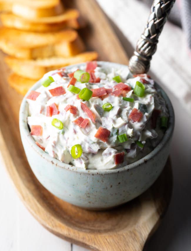 Chipped Beef Dip in a small bowl on a wooden serving platter next to toasted bread. 