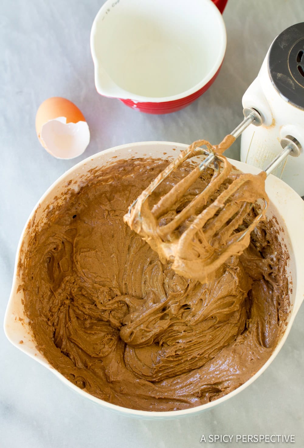 Chocolate cake batter in a mixing bowl next to a hand mixer. 