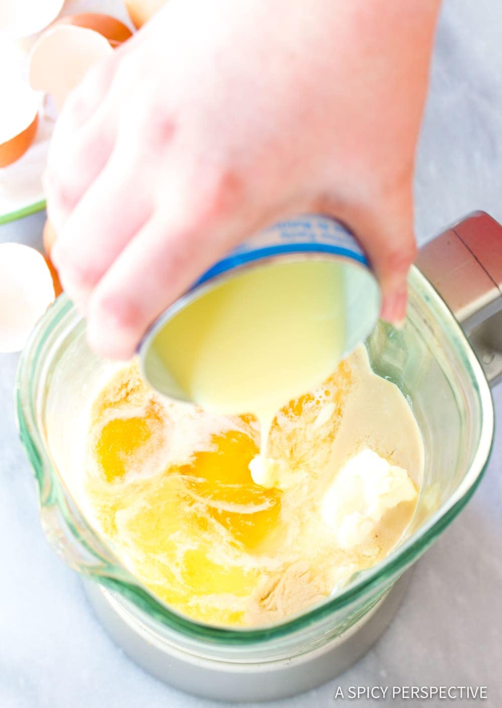 Hand pouring a can of condensed milk into a blender with other ingredients in it. 