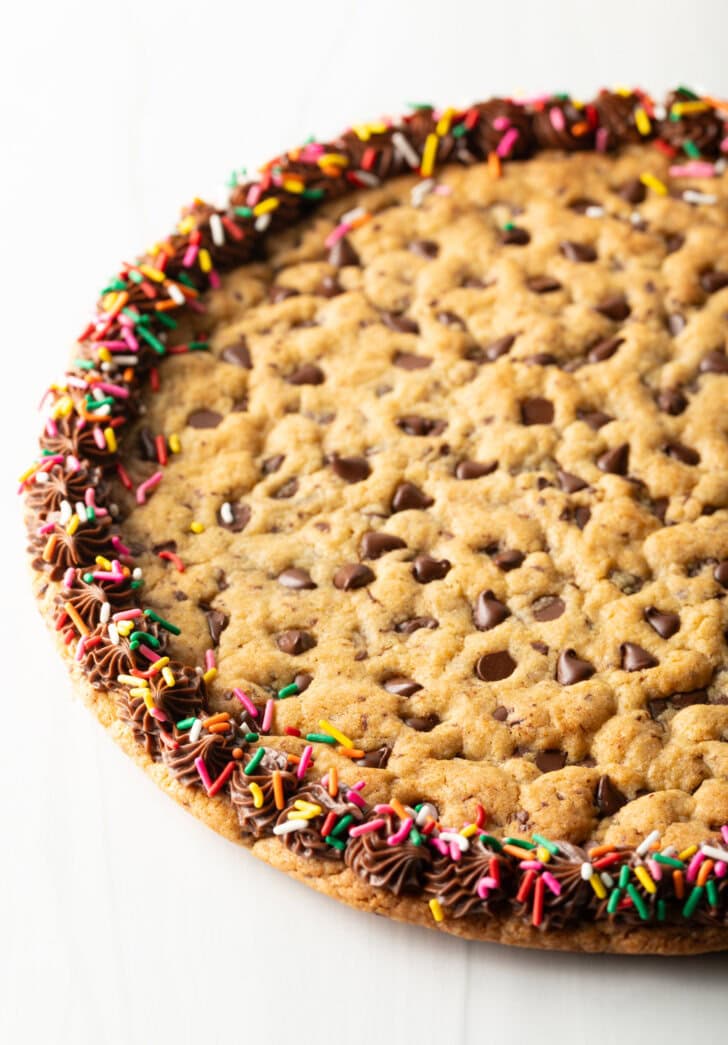 Large chocolate chip cookie cake. The outside edge is piped with chocolate frosting and covered with rainbow sprinkles.