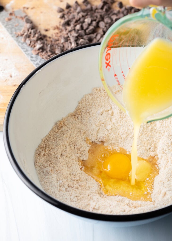 Adding melted butter to the white mixing bowl with dry ingredients