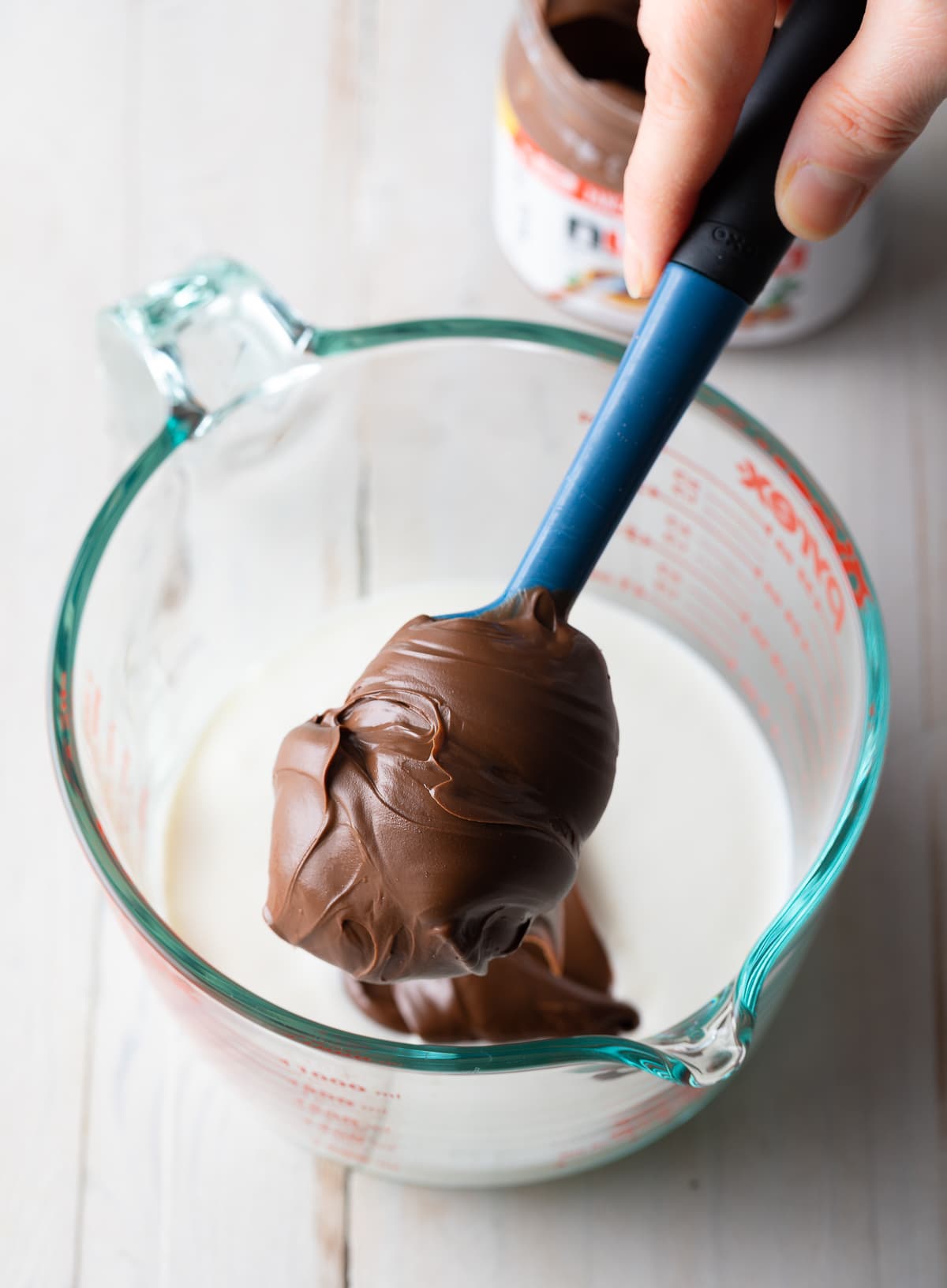 Nutella going into a mixing bowl with cream in it. 