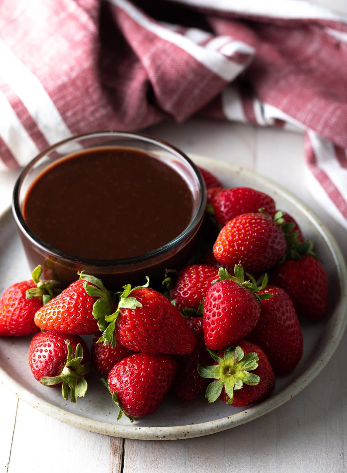 Fresh strawberries on a plate next to a small bowl of nutella chocolate fondue. 