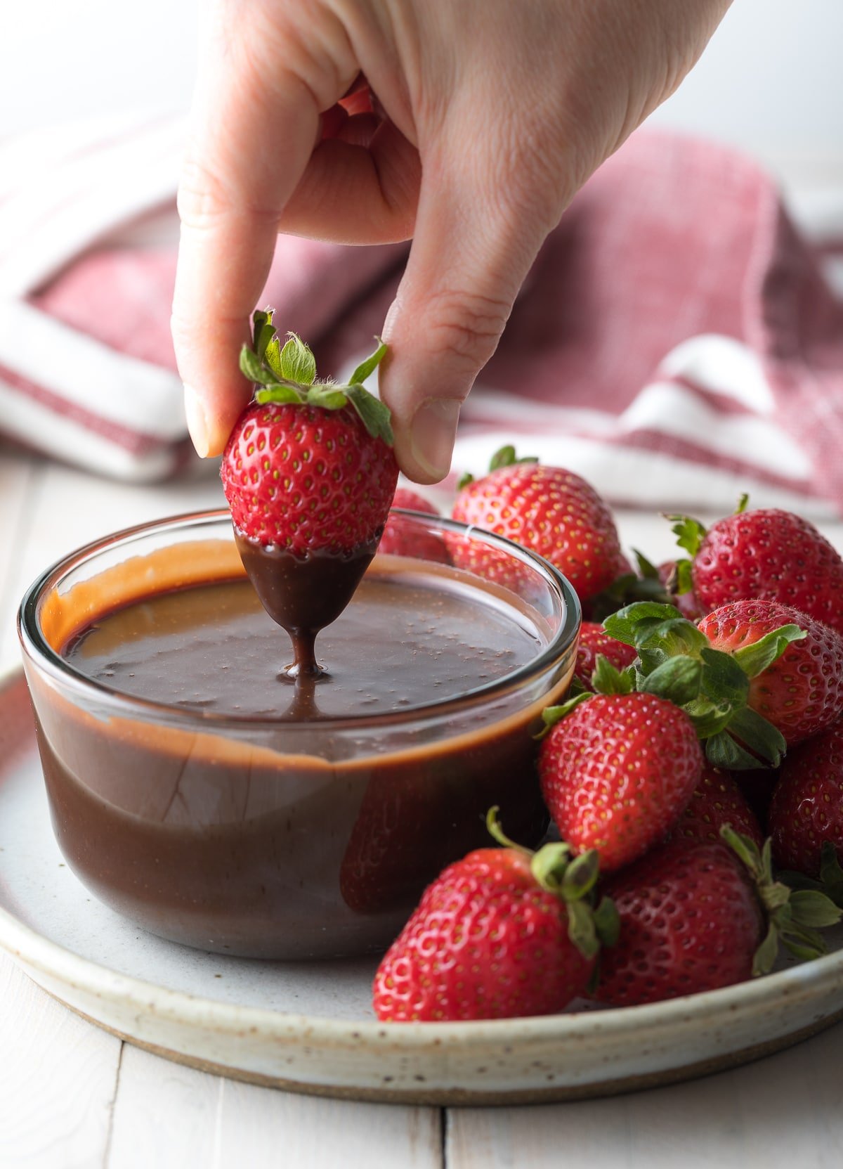 Hand dipping a fresh strawberry into chocolate fondue. 