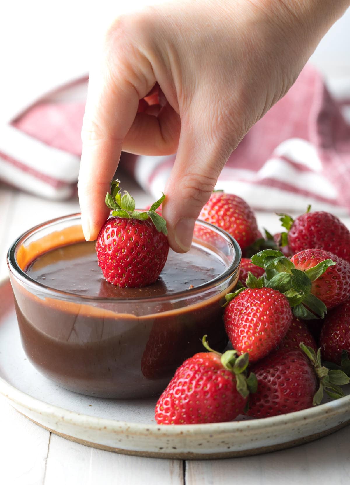 Hand dipping a strawberry into a small bowl of chocolate fondue. 