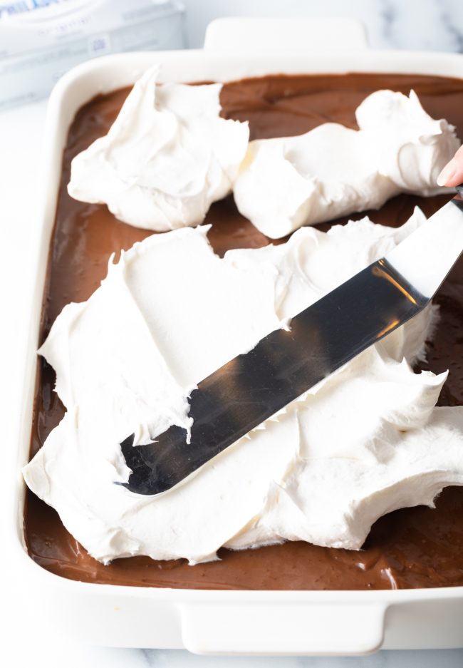 spreading on the final layer of cool whip onto the chocolate lasagna 