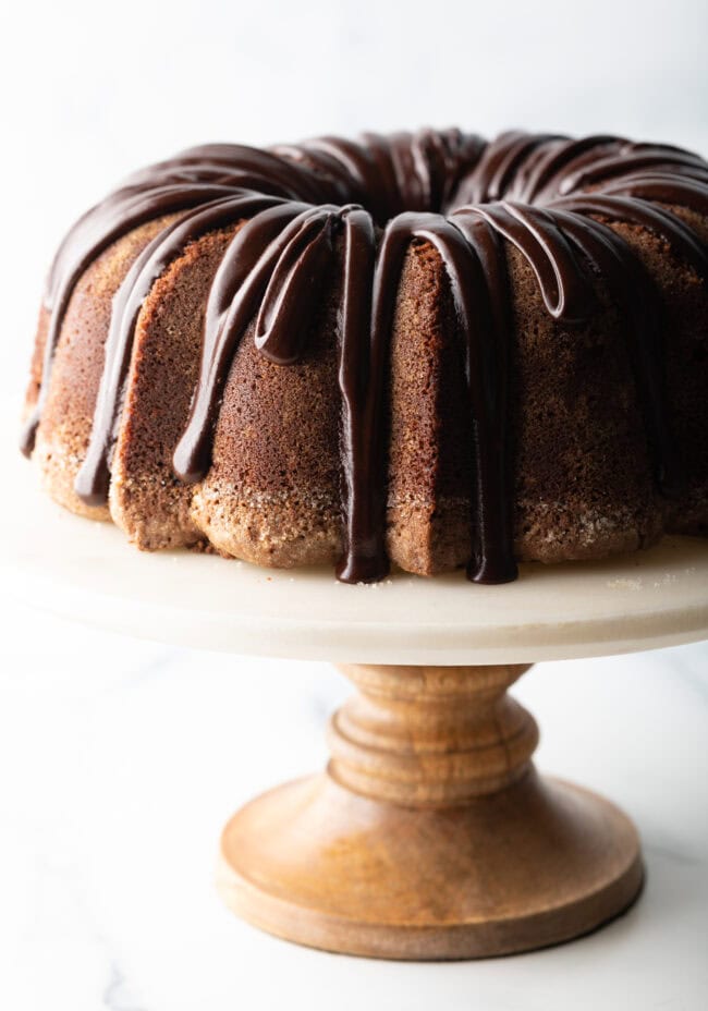 Chocolate Glaze for Pound Cake - Chocolate sour cream bundt cake with a thick chocolate glaze drizzled on top. The cake is on a white stand.