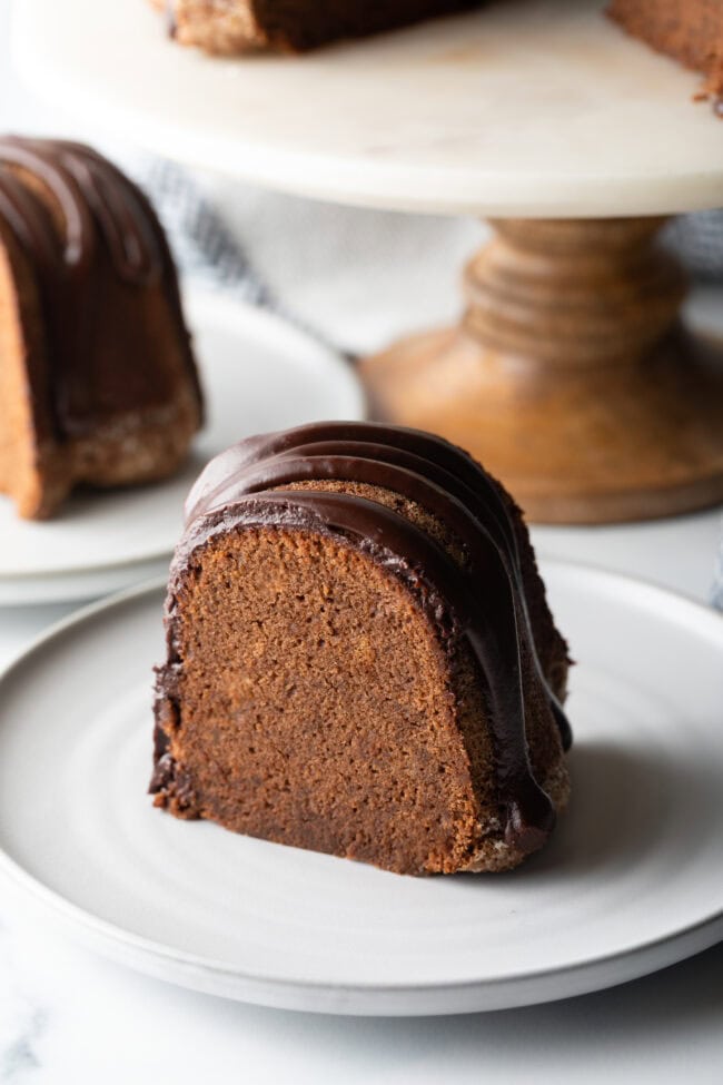 Thick slice of chocolate sour cream pound cake with drizzle of glaze on a white plate.